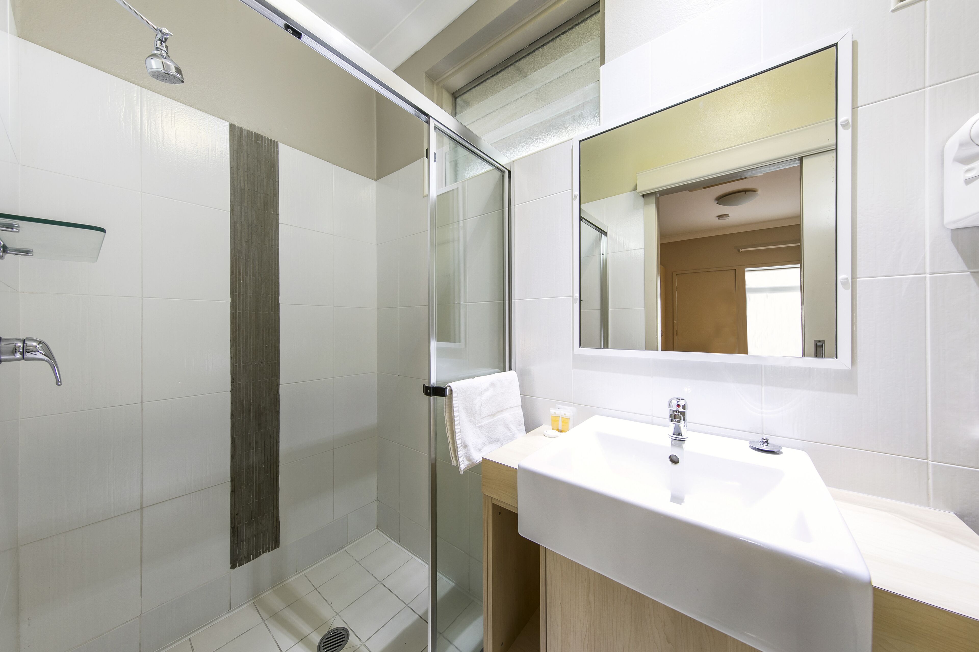 Une salle de bain moderne avec une douche à l’italienne en verre, un lavabo blanc et un miroir au-dessus.