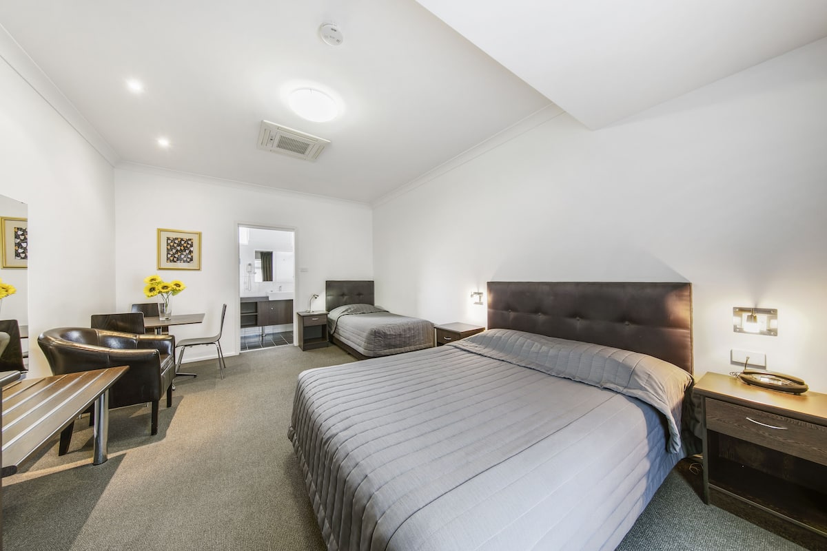 A modern hotel room with a large bed, a desk, a chair, and a small table.