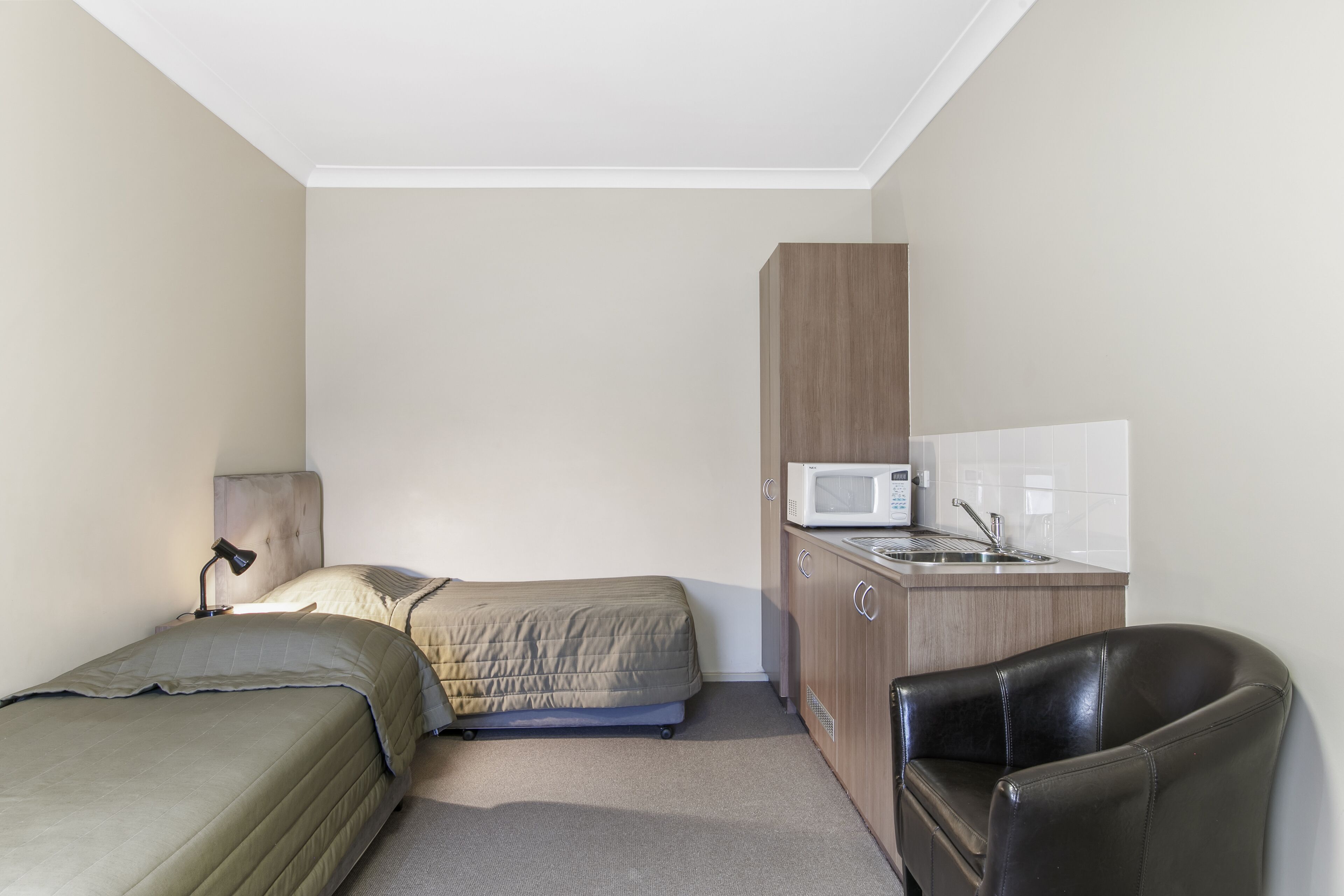Una habitación pequeña con cama, escritorio con silla, microondas y lavamanos.