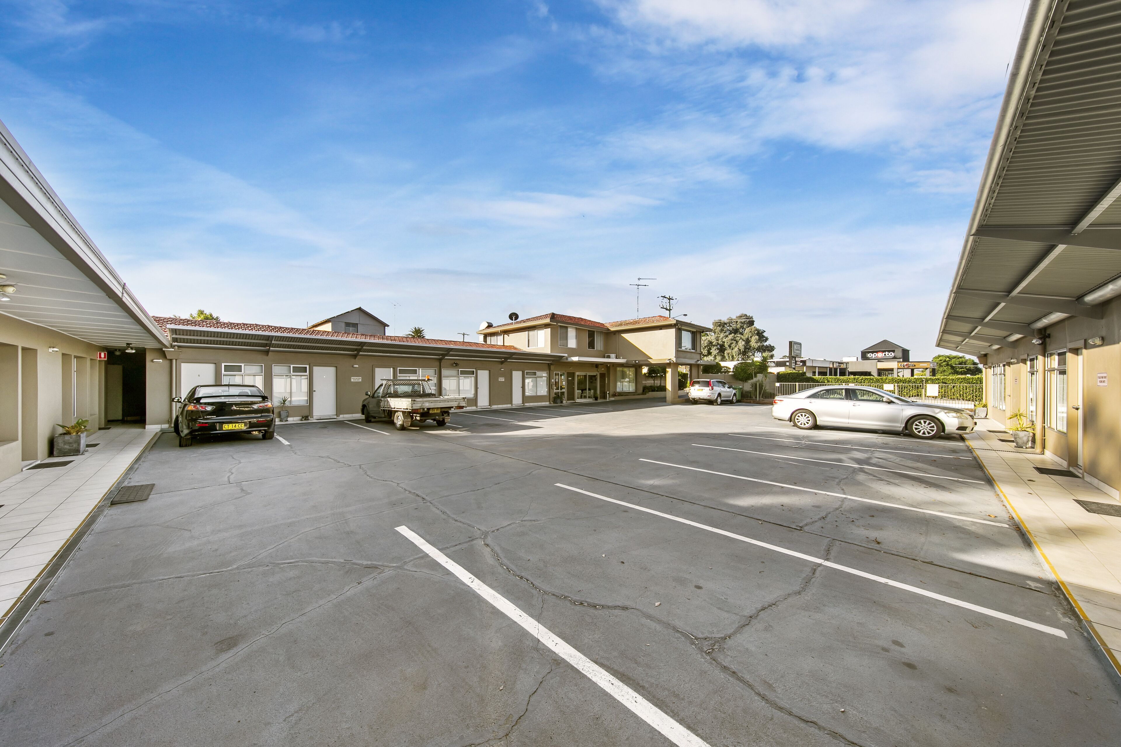 A parking lot with a few cars, a truck, and a building with a sign that reads "Optico".