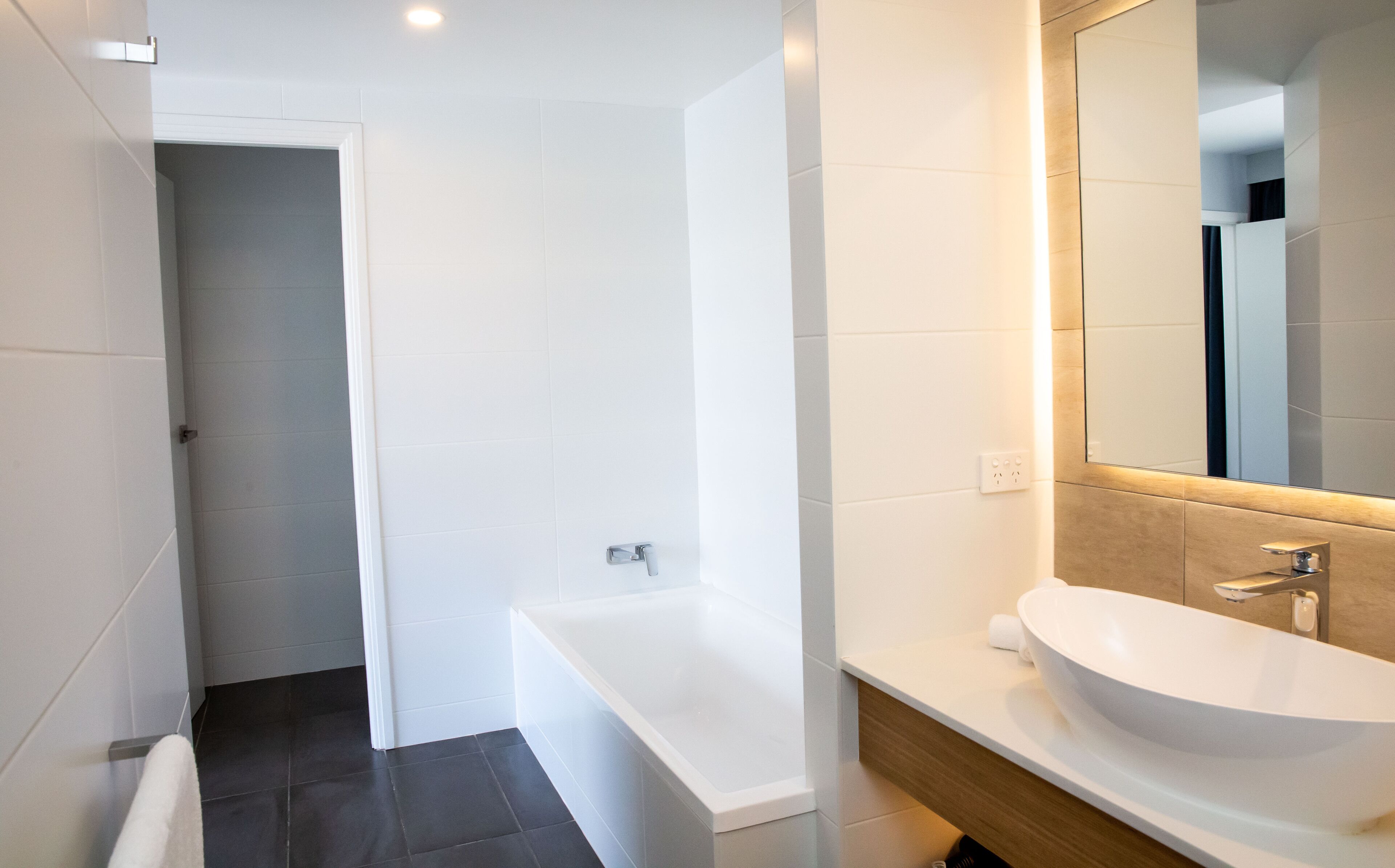 A modern bathroom with a white bathtub, a large mirror, and a white sink.