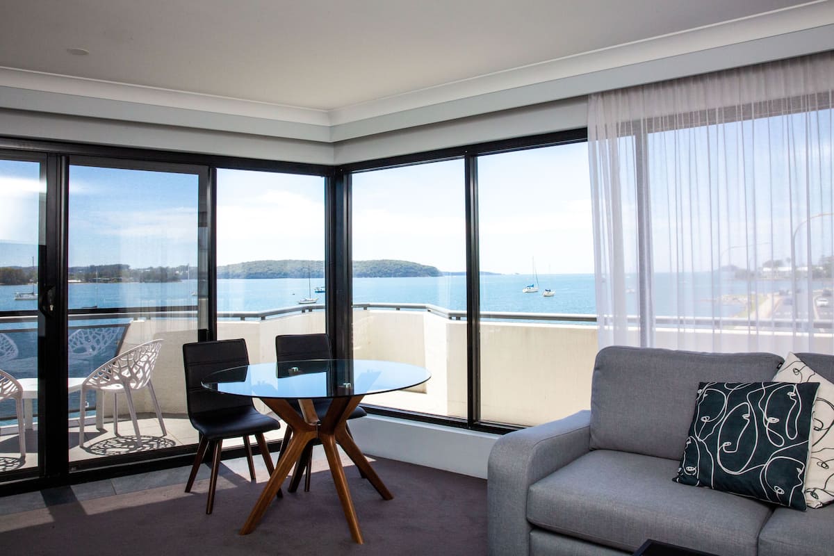 A modern room with a balcony, a round table with chairs, and a sofa with decorative pillows.