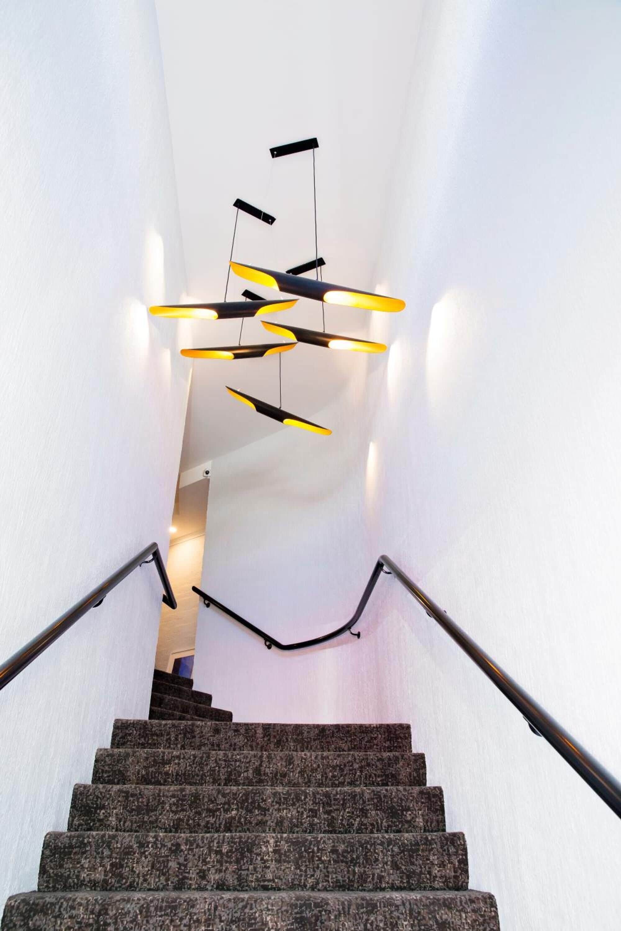A staircase with a modern design, featuring a handrail on both sides and a unique lighting fixture above.