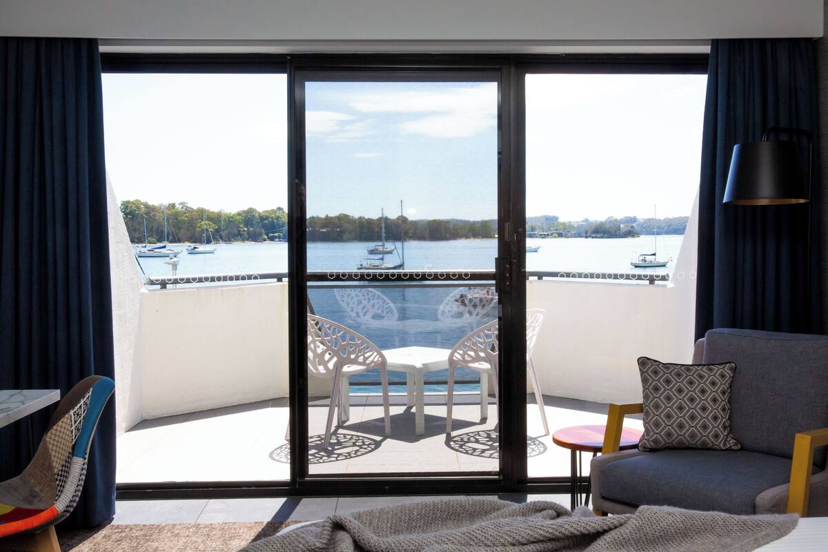 A balcony with a view of the water, a table, chairs, and a sofa.
