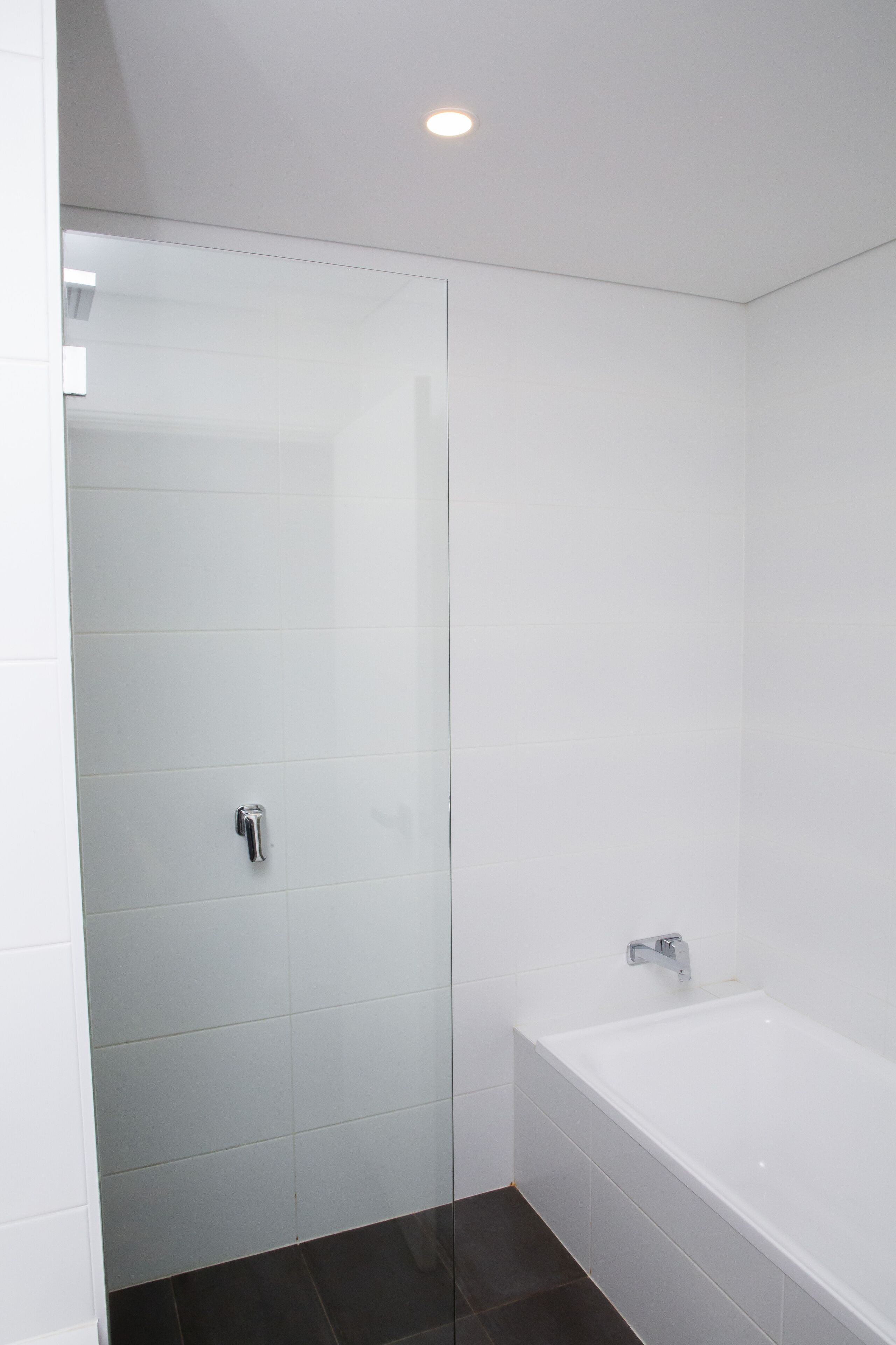 Un baño moderno con azulejos blancos, una mampara de cristal y una bañera blanca.
