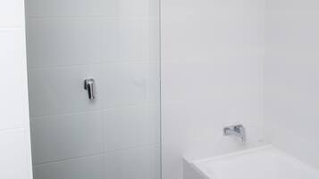 A modern bathroom with white tiles, a glass shower door, and a white bathtub.