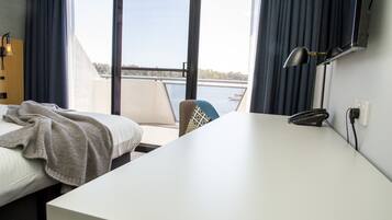 A hotel room with a bed, a desk, a chair, and a view of a body of water through large windows.