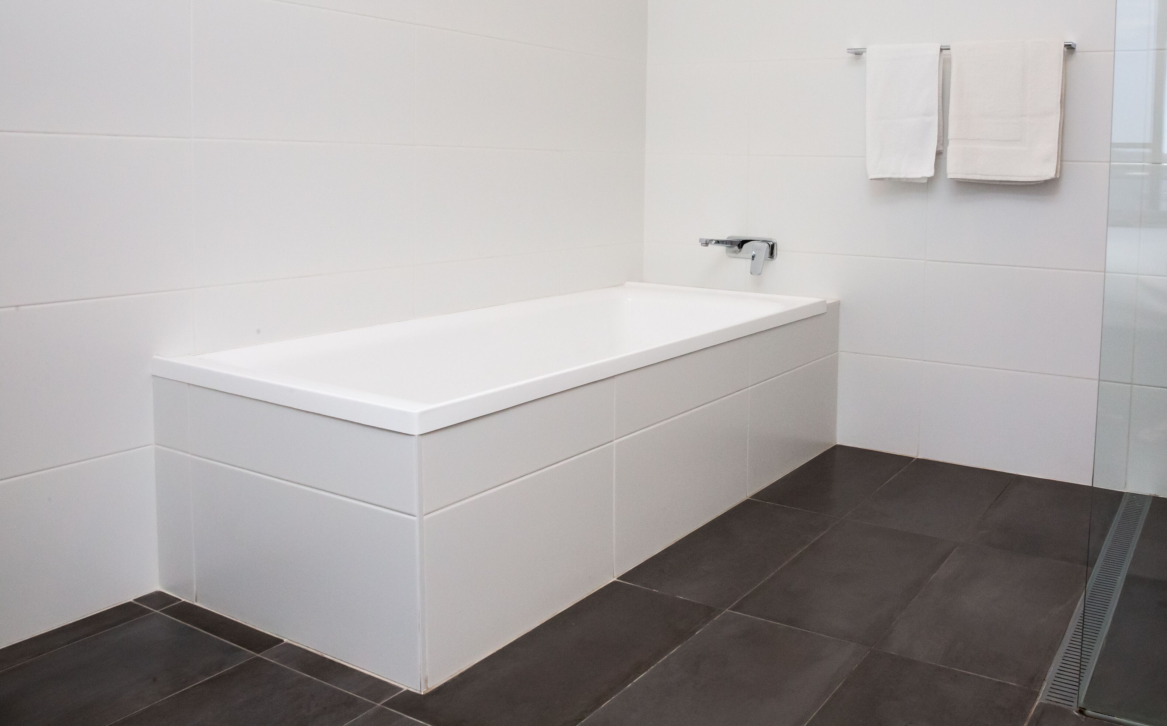 A modern bathroom with a white bathtub, dark floor tiles, and white wall tiles.