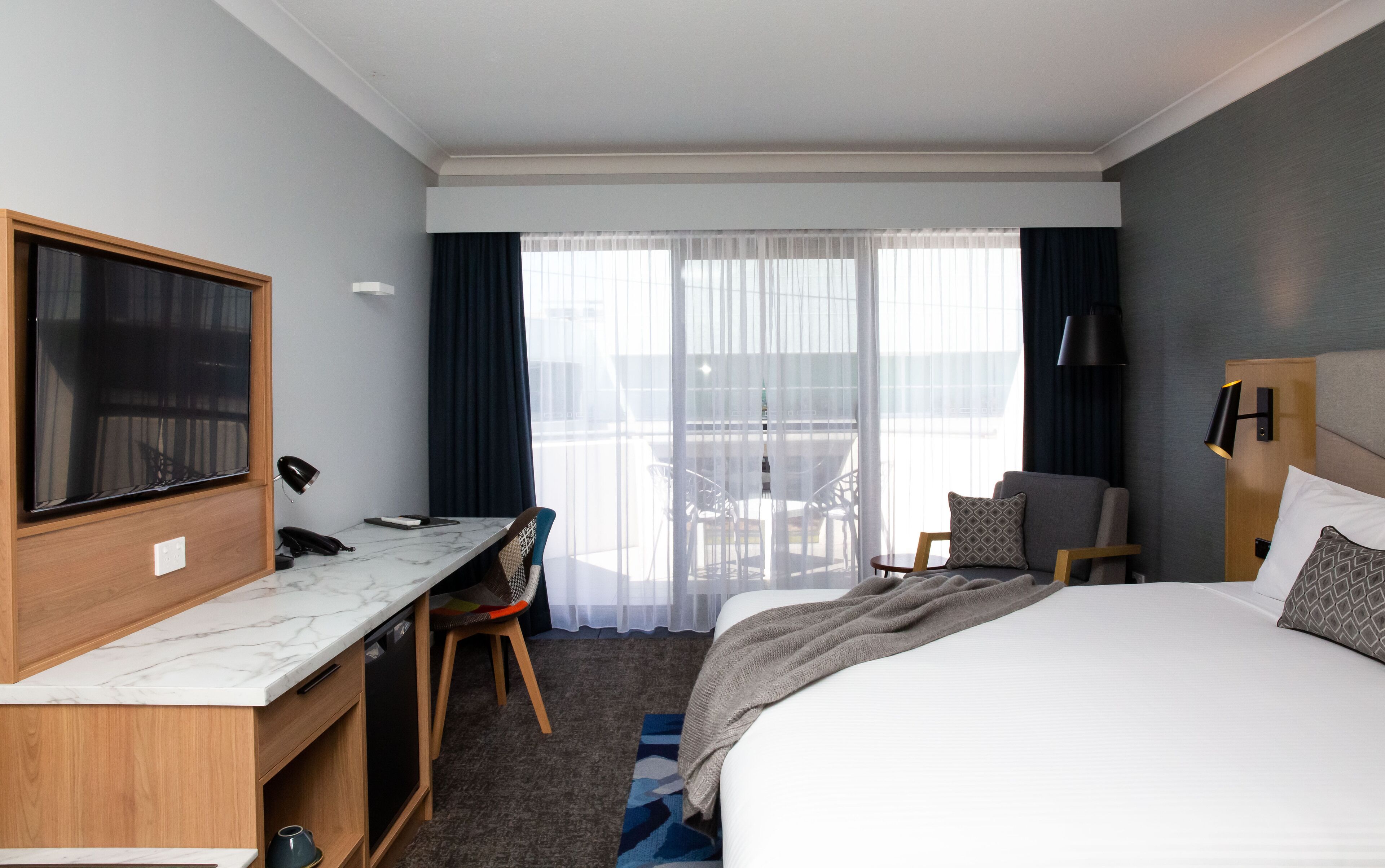 Ein Hotelzimmer mit Bett, Schreibtisch, Stuhl, Fernseher und einem Fenster mit Vorhängen.