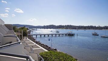 Enjoy breathtaking views of the calm water from this waterfront property's balcony, overlooking a serene landscape with a pier and boats.