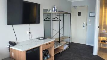 Una camera d'albergo moderna con TV a schermo piatto, una toeletta in legno con lavandino, un frigorifero compatto e un piccolo cestino.