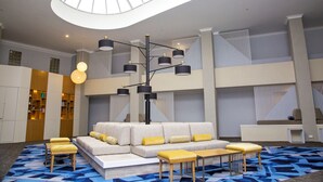A spacious lobby with a modern sofa, wooden stools, and a unique ceiling light fixture. - The Esplanade (Batemans Bay)