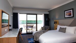 A hotel room with a bed, a desk with a chair, a desk lamp, a telephone, a window with curtains, and a view of the outside balcony. - The Esplanade (Batemans Bay)