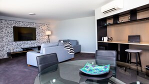A modern living room with a glass dining table, a sofa, a TV, and a desk with a laptop. - The Esplanade (Batemans Bay)