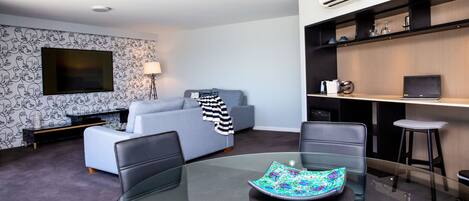 A modern living room with a glass dining table, a sofa, a TV, and a desk with a laptop.