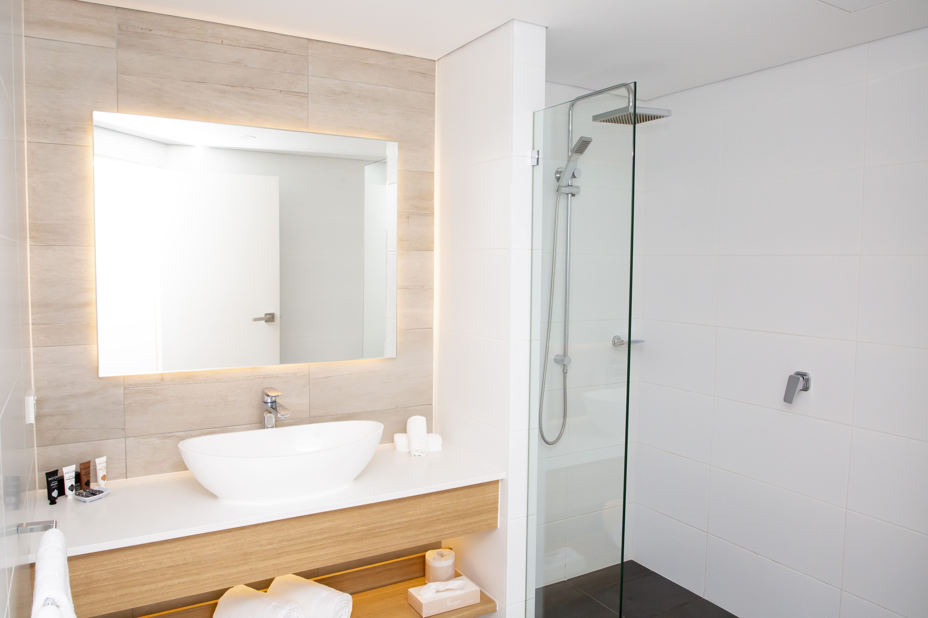 A modern bathroom with a large mirror, white sink, and glass-enclosed shower.