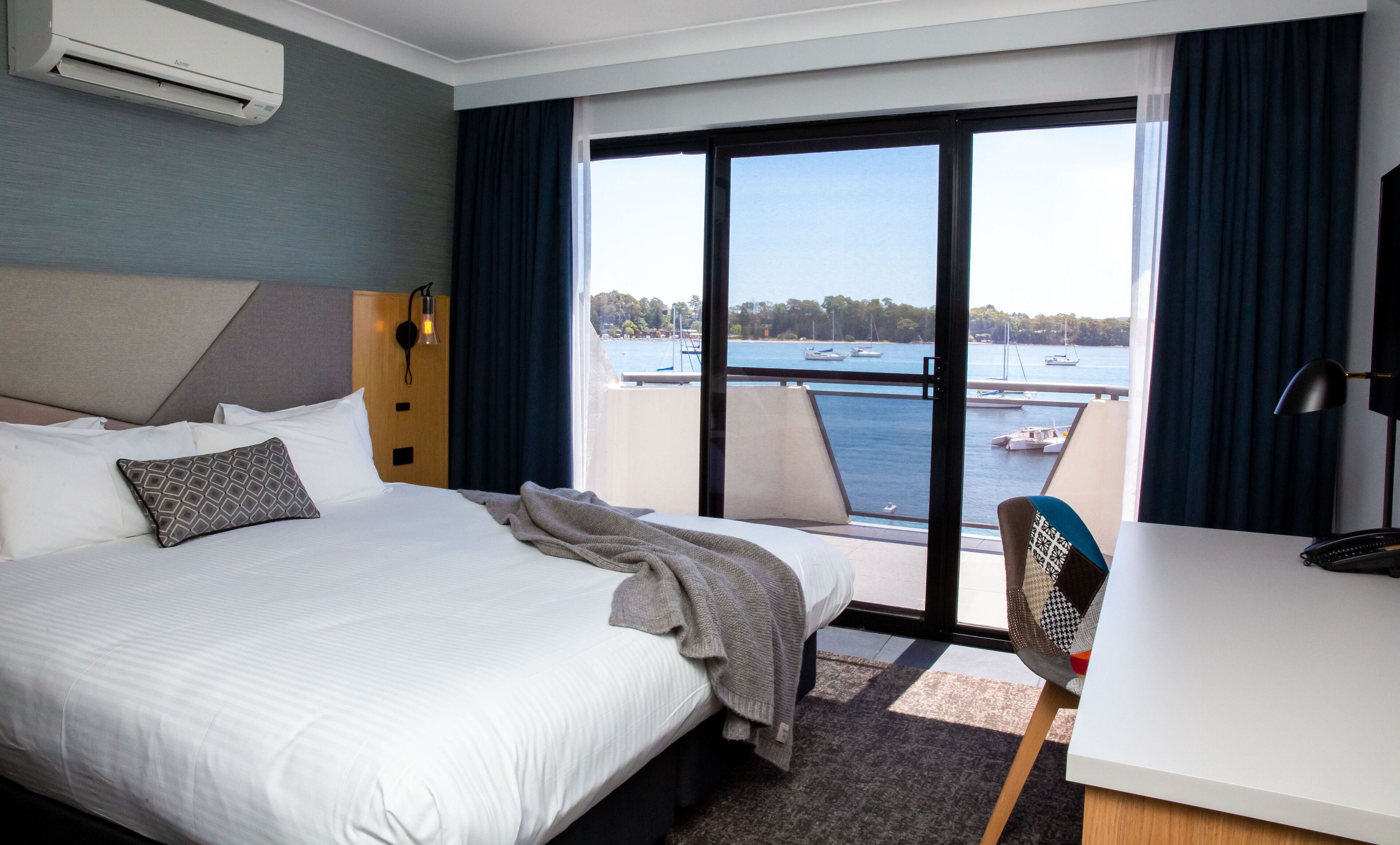 Habitación de hotel con cama, escritorio, silla, vista al mar y balcón.