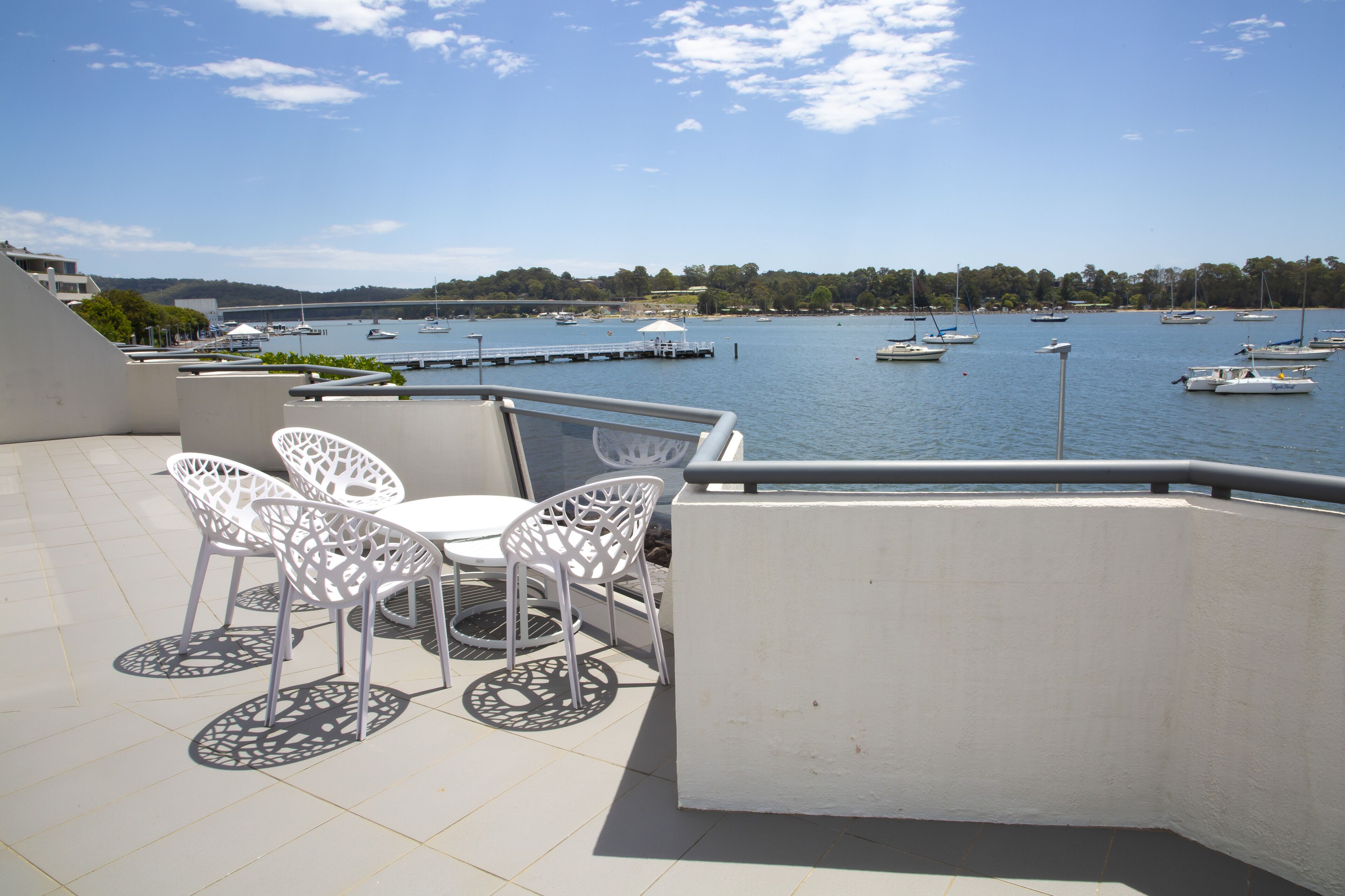 Una terraza con sillas blancas y una mesa con vista a un puerto deportivo con barcos.
