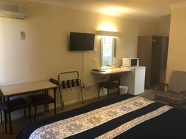 Habitación de hotel con cama, escritorio, silla, televisor, microondas y una pequeña kitchenette.