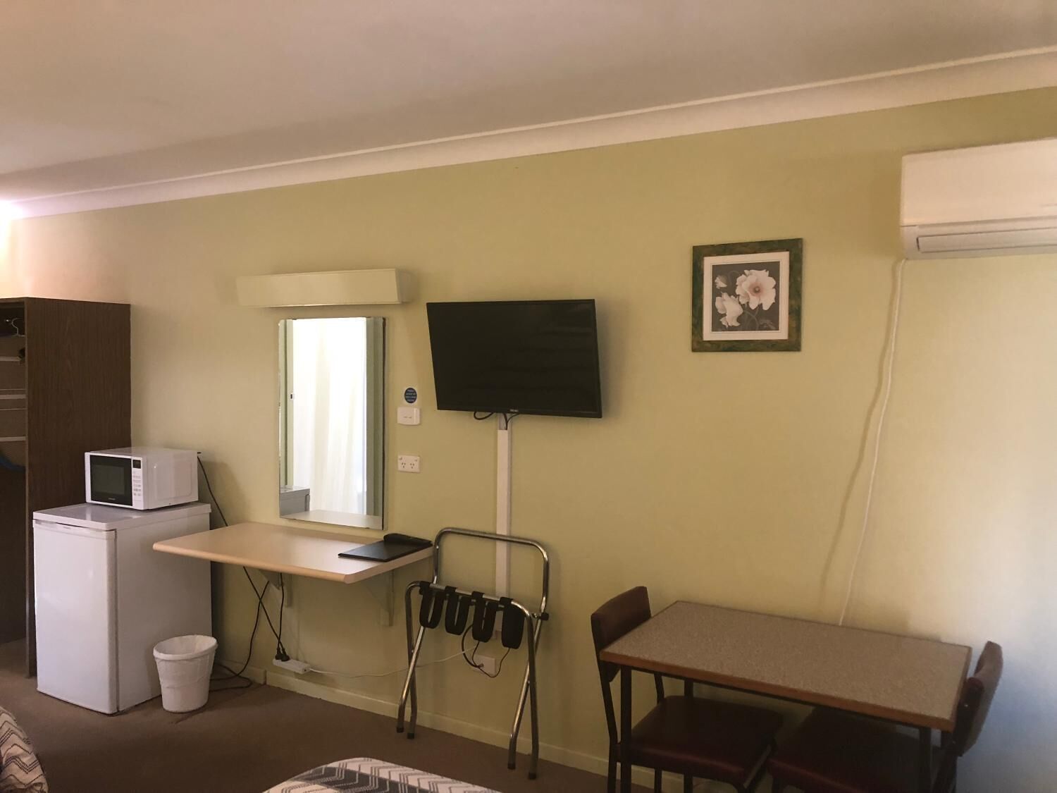 Une chambre compacte comprenant un coin cuisine, un téléviseur fixé au mur, une petite table avec deux chaises et un lit simple.