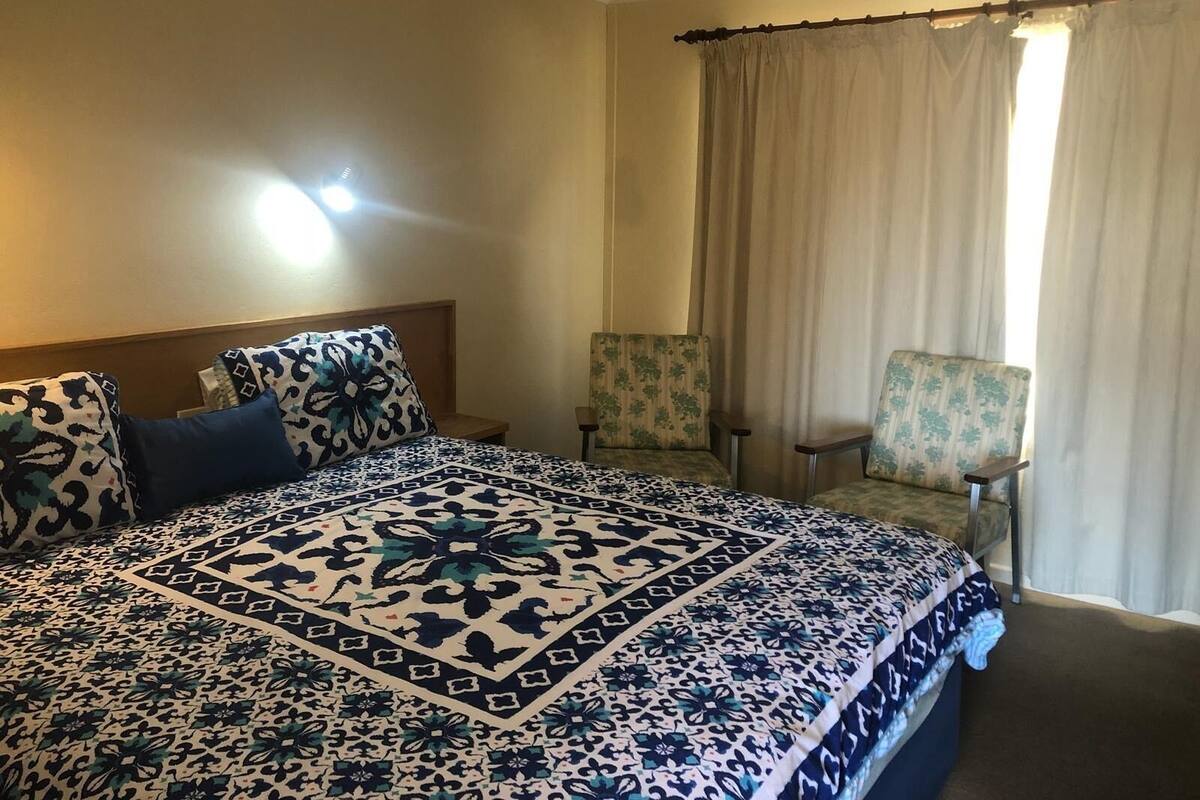 A hotel room with a large bed, two chairs, a nightstand, and a window with curtains.
