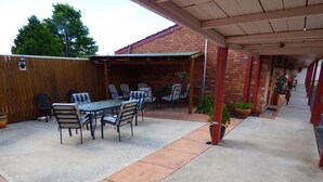 An outdoor patio with a table and chairs, a wooden fence, and a brick building in the background.