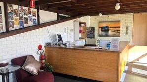 A reception area with a wooden desk, a computer, a fire extinguisher, a red chair, and a wall with movie posters.