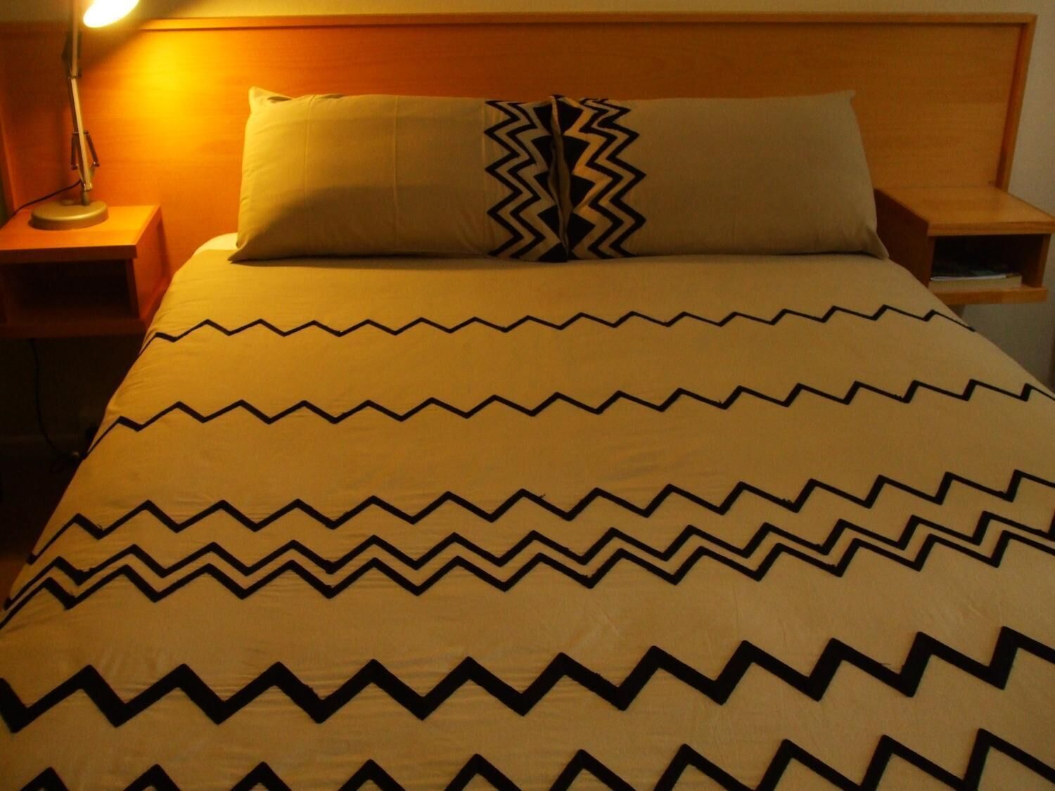 A bed with a patterned bedspread and two pillows, one with a zigzag design.