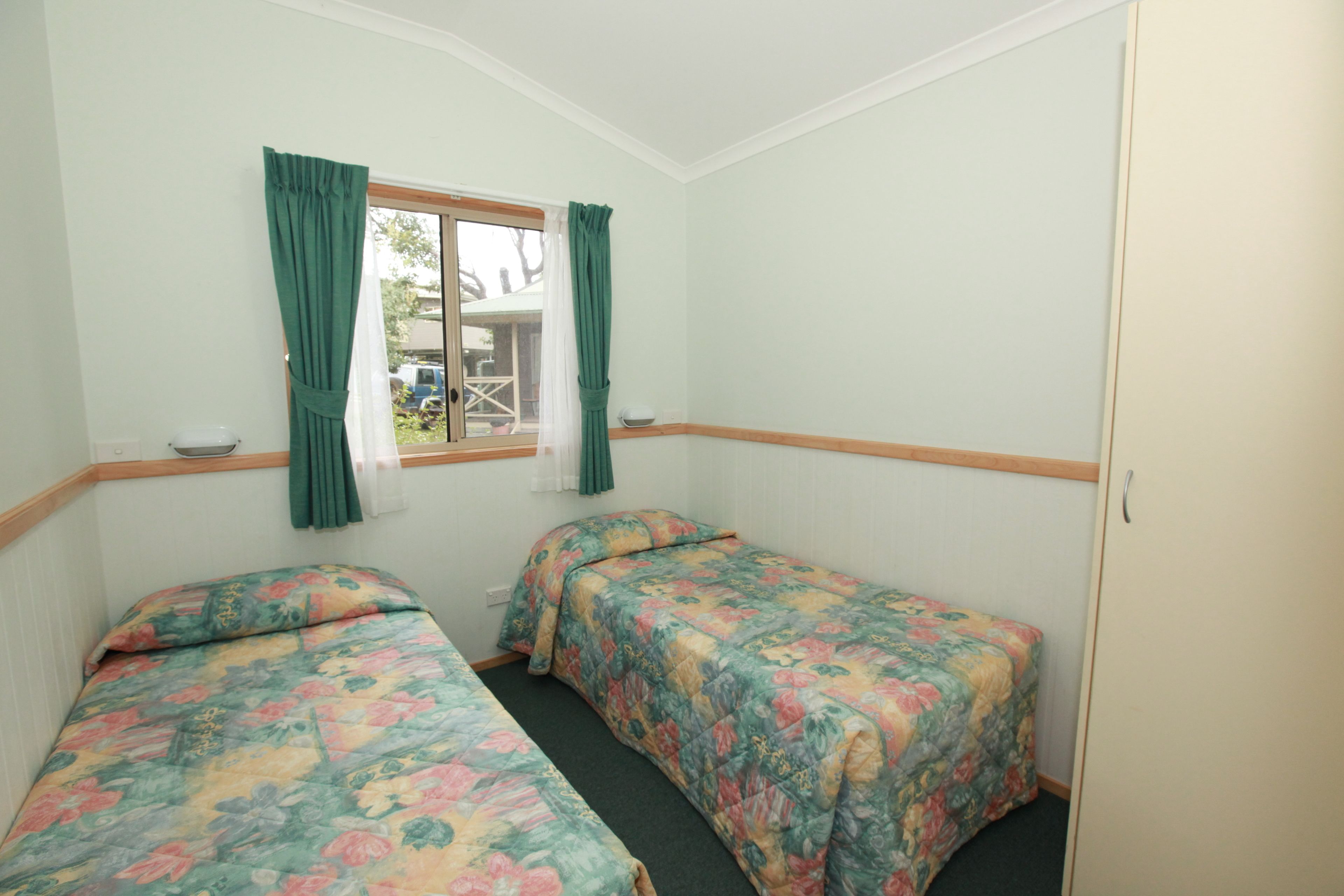 Une chambre avec deux lits simples, chacun agrémenté d’une literie à motifs floraux, une fenêtre avec des rideaux et une vue sur l’extérieur.