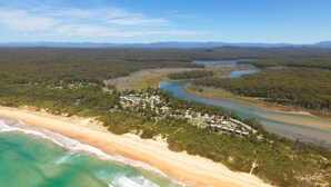 Vista aérea de una zona costera con playa, un río y una región boscosa con un conjunto de edificios.