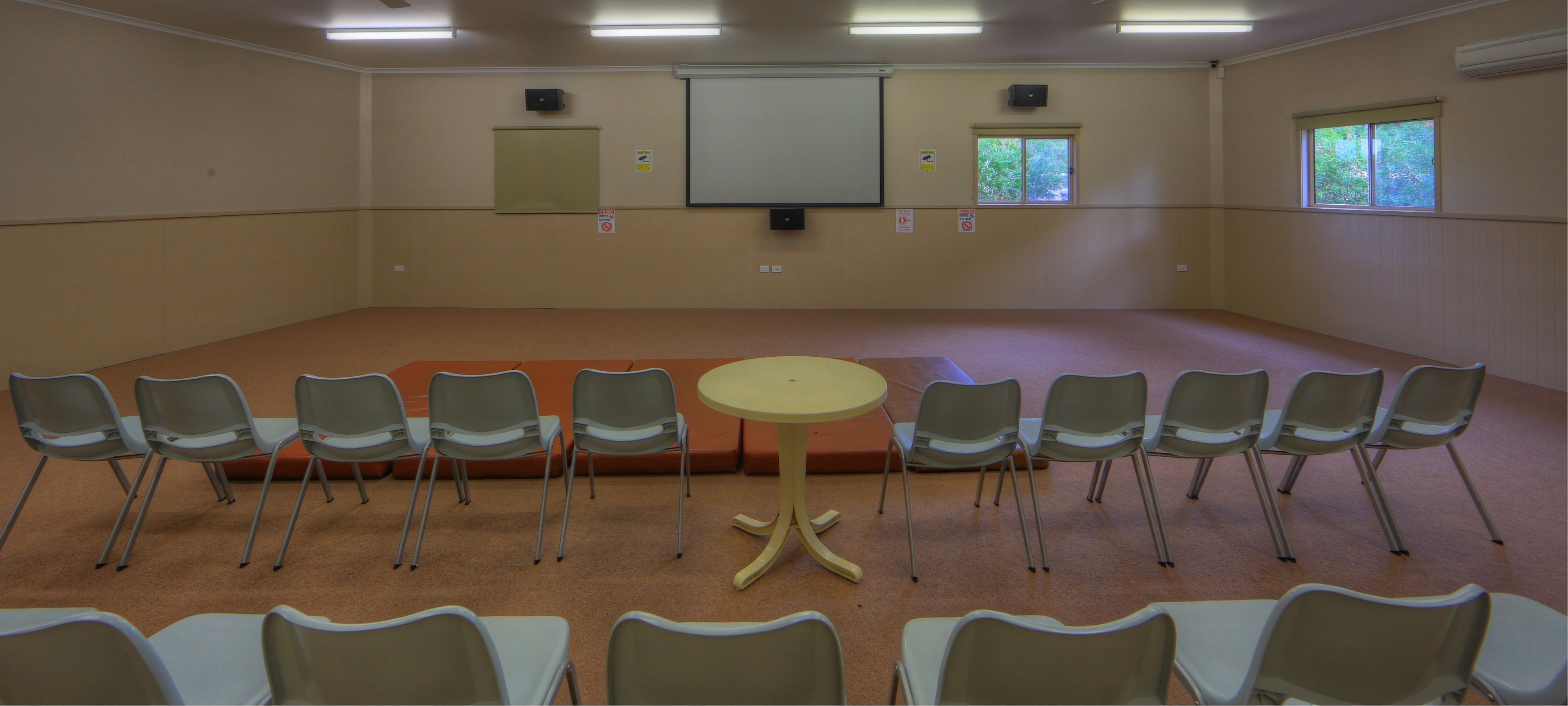 Une salle de conférence équipée d’un grand écran, d’un projecteur et d’une petite table.