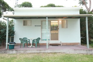 A small, single-story building with a covered porch, a bench, and two chairs. - Lakesea Park (South Durras)