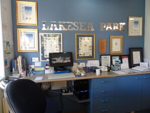 A reception desk with framed awards, a computer, and a chair. - Lakesea Park (South Durras)