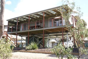 A two-story house with a covered balcony, a staircase leading to the upper level, and a car parked in the driveway. - Lakesea Park (South Durras)