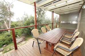 A covered outdoor dining area with a wooden table and wicker chairs, overlooking a garden. - Lakesea Park (South Durras)