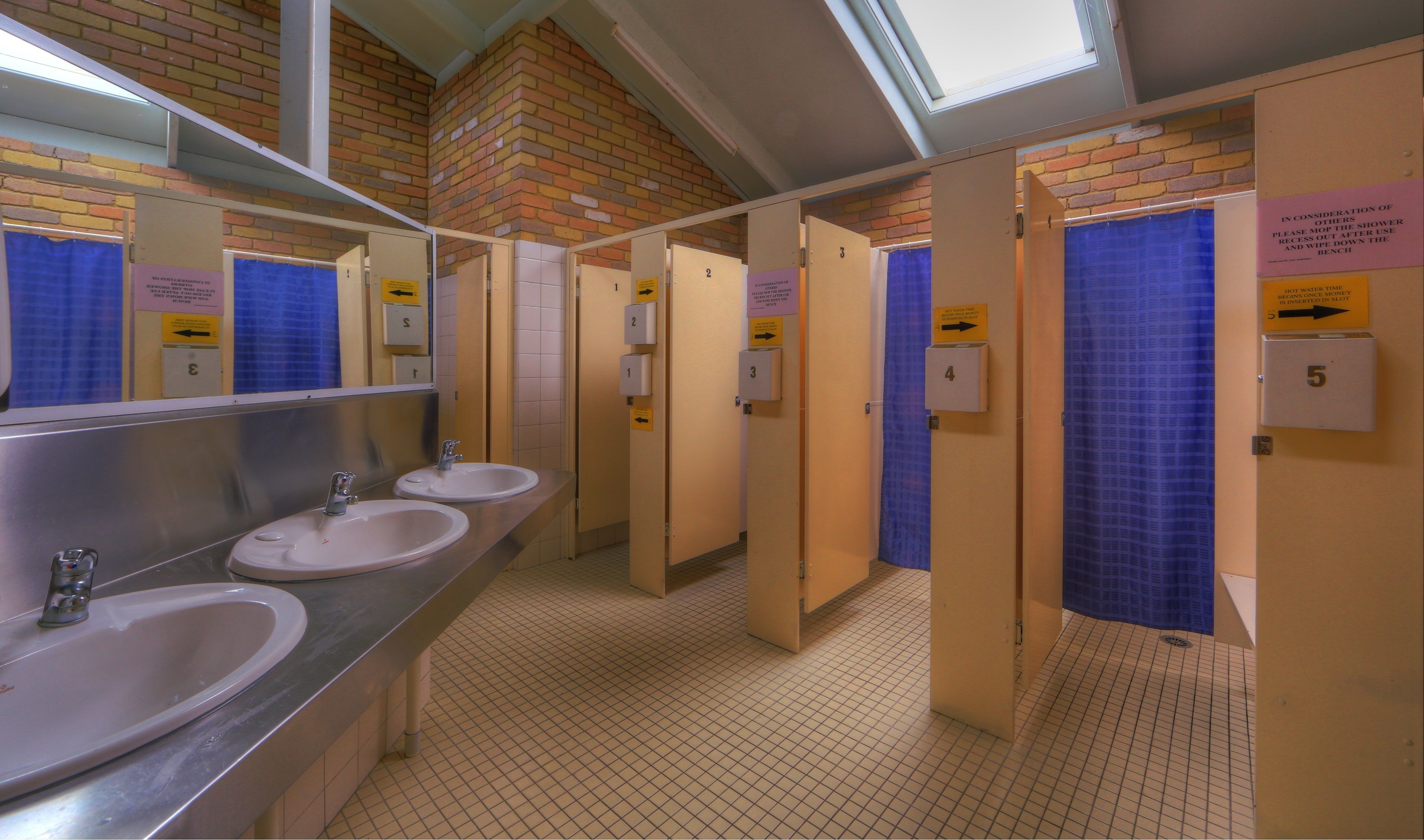 A public restroom with multiple sinks, numbered stalls, and a mirror.