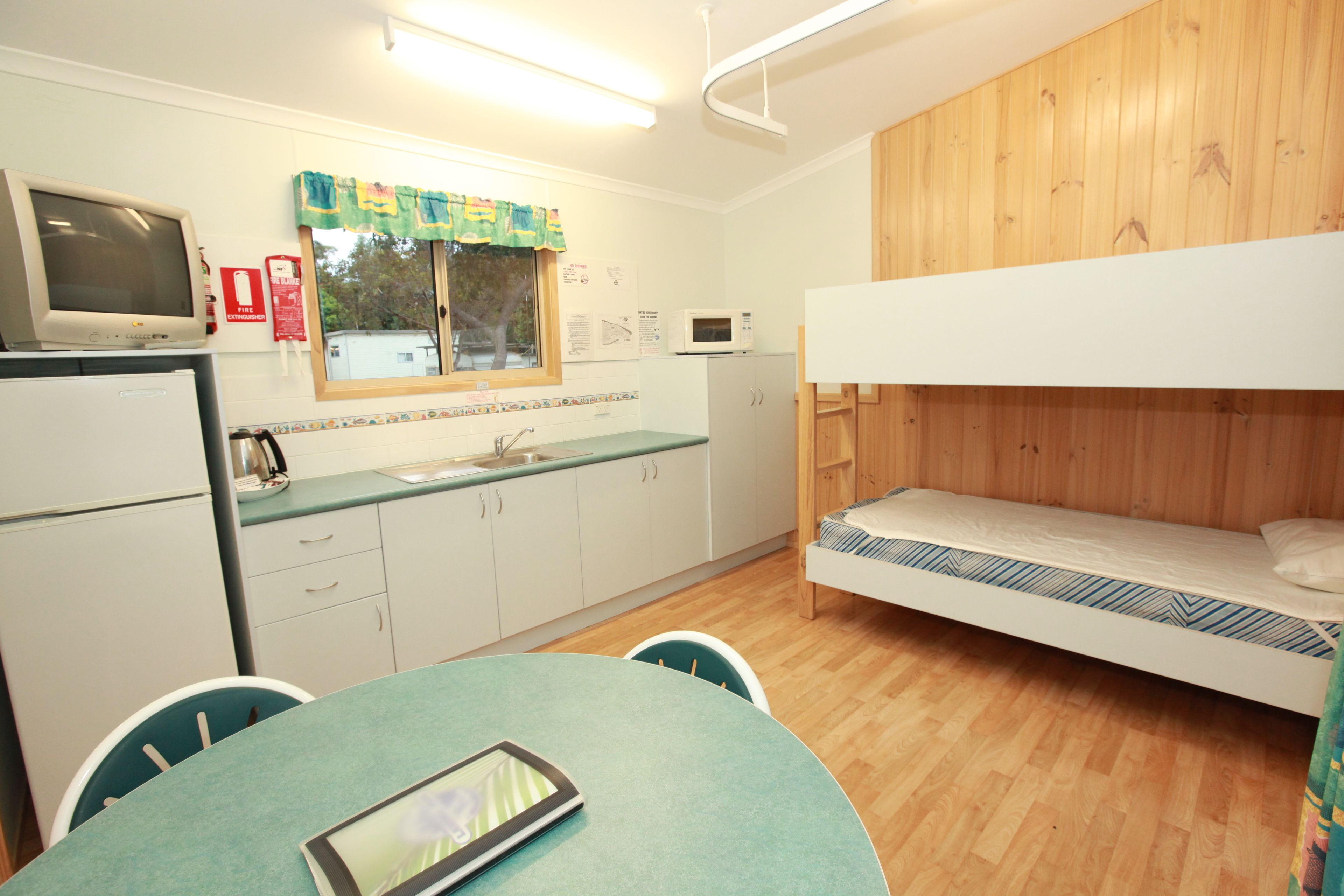 Una habitación compacta con literas, una kitchenette con microondas, refrigerador y una ventana con cortina.