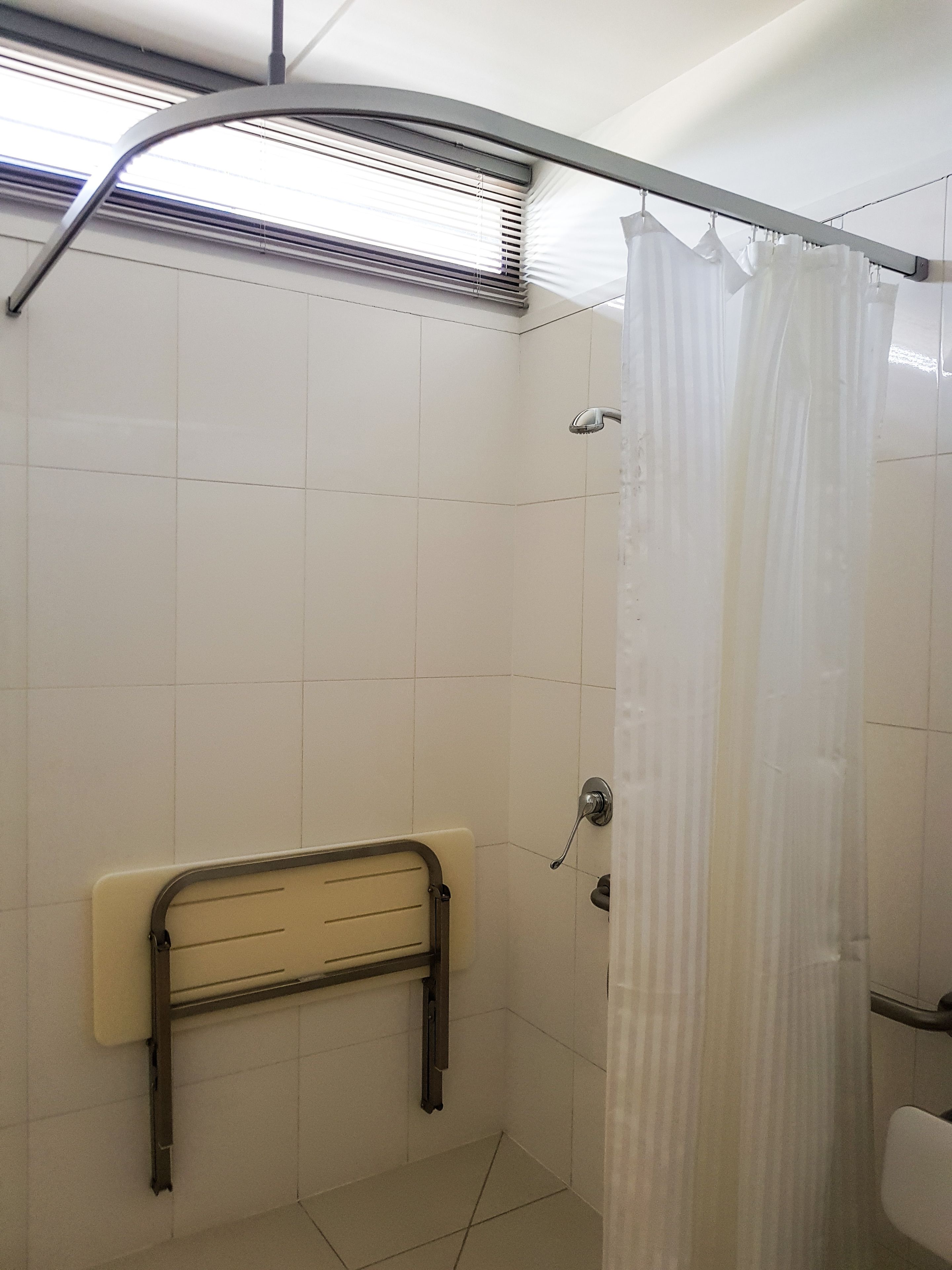 Een badkamer met douche, toilet en een handgreep.