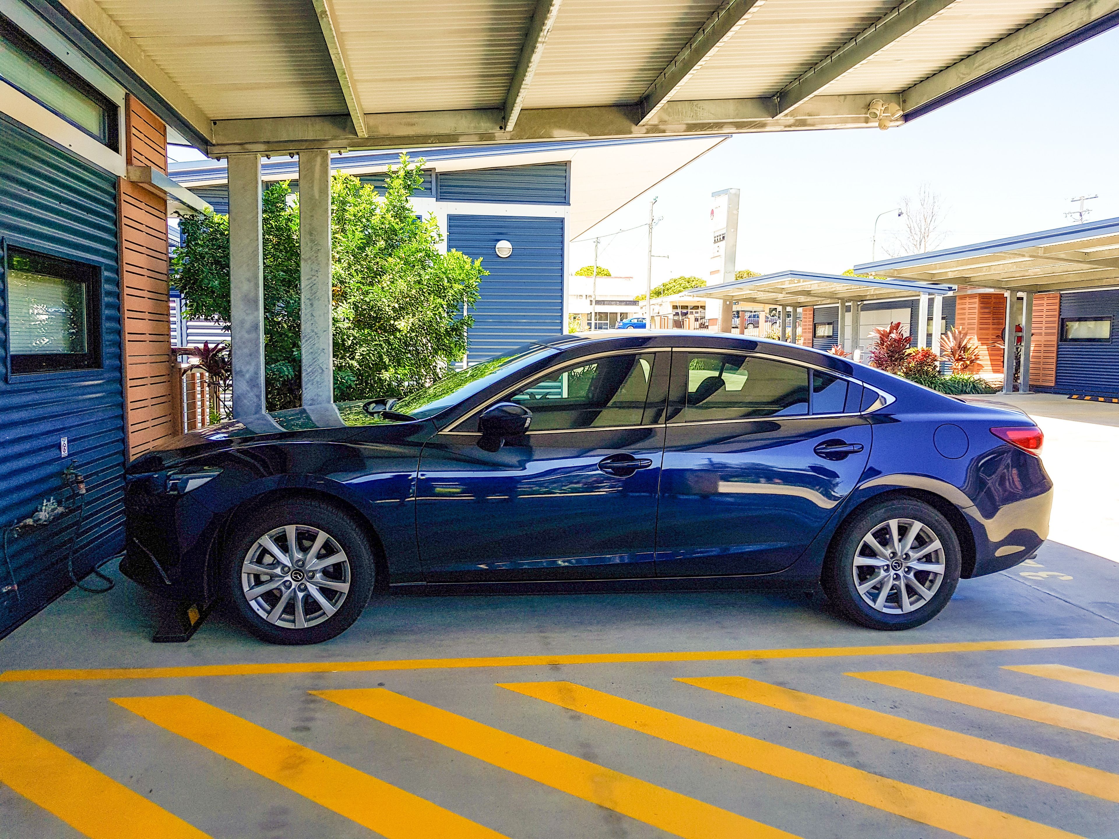 Une voiture bleue est garée sous un abri, avec un bâtiment en arrière-plan.