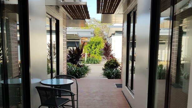 A covered outdoor corridor with a wooden deck, glass doors, and a small table with chairs. - Moura Meridian Motel (Moura)
