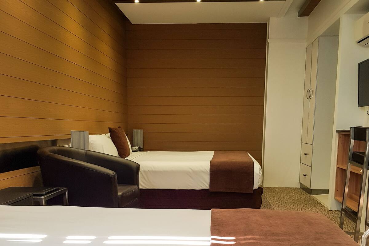 A hotel room with two beds, a sofa, a wardrobe, and a television.
