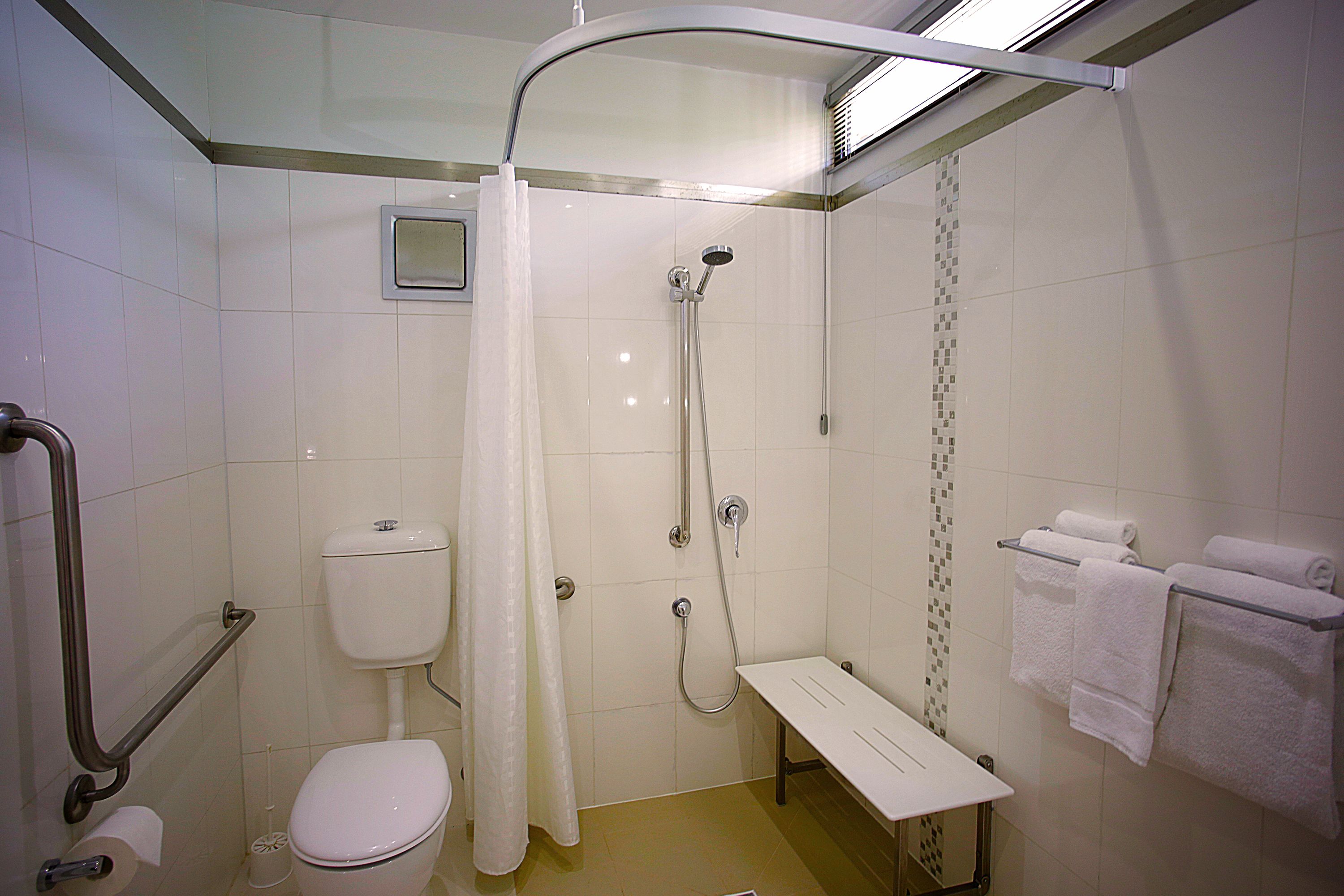 A small, modern bathroom with a shower, toilet, and a bench.