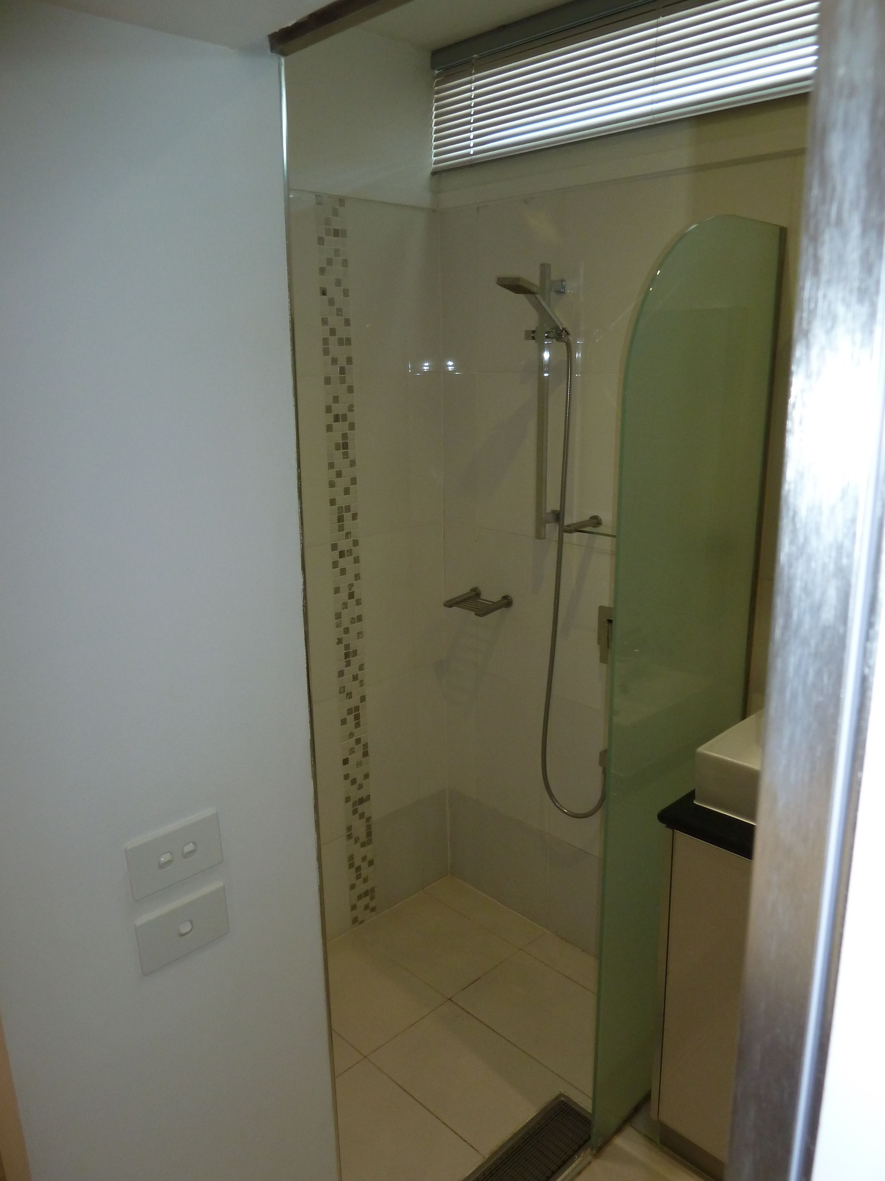 Ducha envuelta en vidrio con cabezal de ducha de mano y llave instalada en la pared.