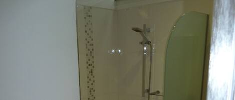 Ducha envuelta en vidrio con cabezal de ducha de mano y llave instalada en la pared.