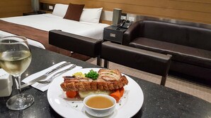A hotel room with a bed, a dining table with a plate of food, a glass of wine, and a couch. - Moura Meridian Motel (Moura)