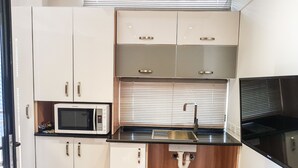 A compact kitchen with white cabinets, a microwave, a sink, and a black countertop. - Moura Meridian Motel (Moura)