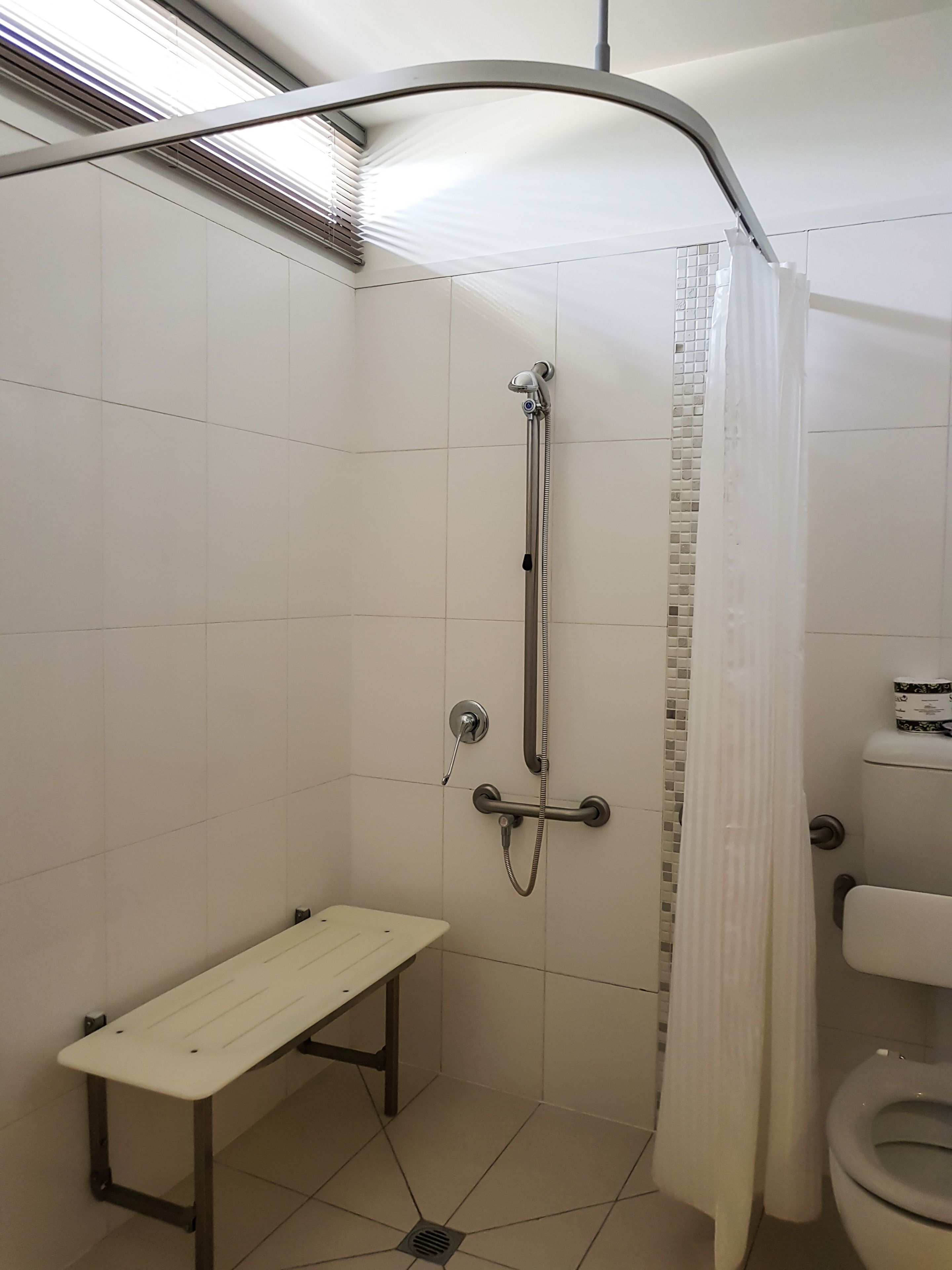 A small, enclosed shower area with a bench, a toilet, and a showerhead.