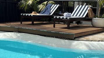 A pool area with two lounge chairs and a potted plant.