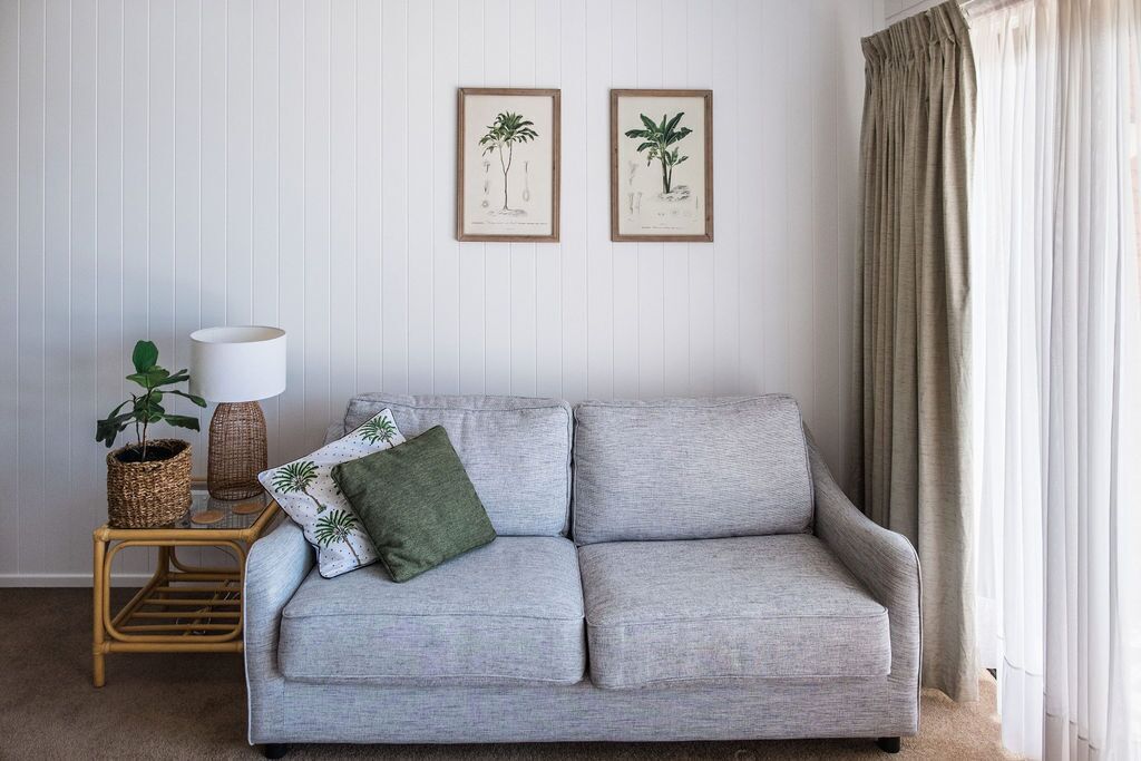 A living room with a grey sofa, two framed botanical illustrations, a lamp, and a potted plant.