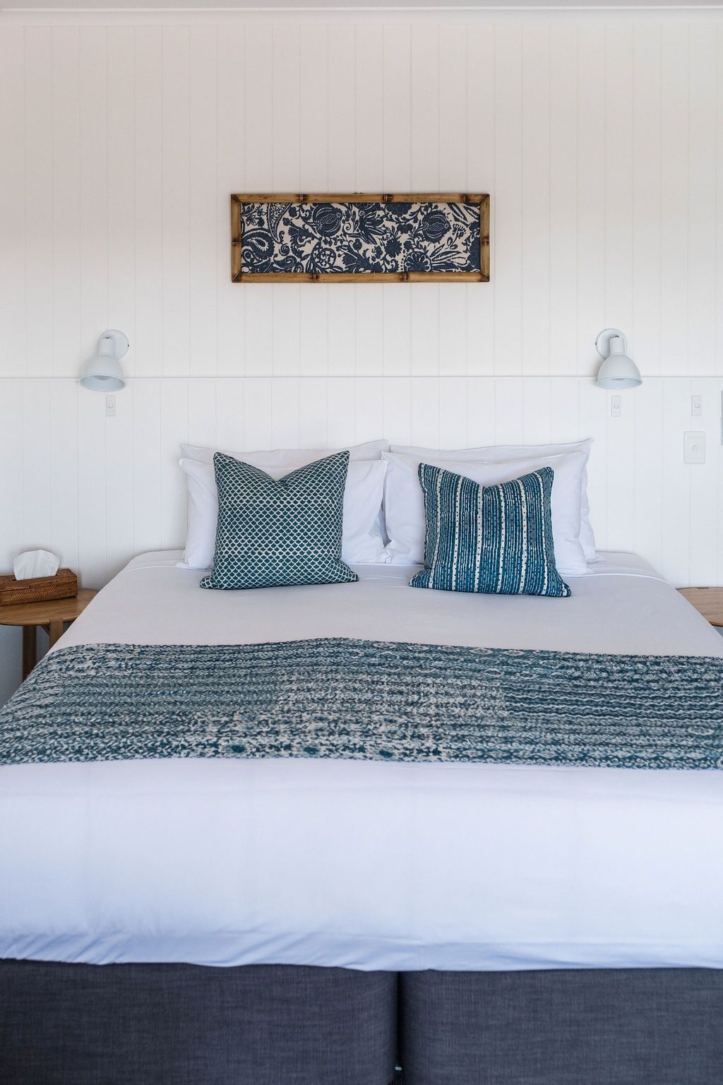 Una cama bien tendida con almohadas blancas y estampadas, una colcha azul y blanca y un adorno decorativo en la pared.